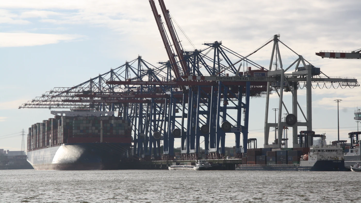 A container ship at a port quay beneath tall loading cranes